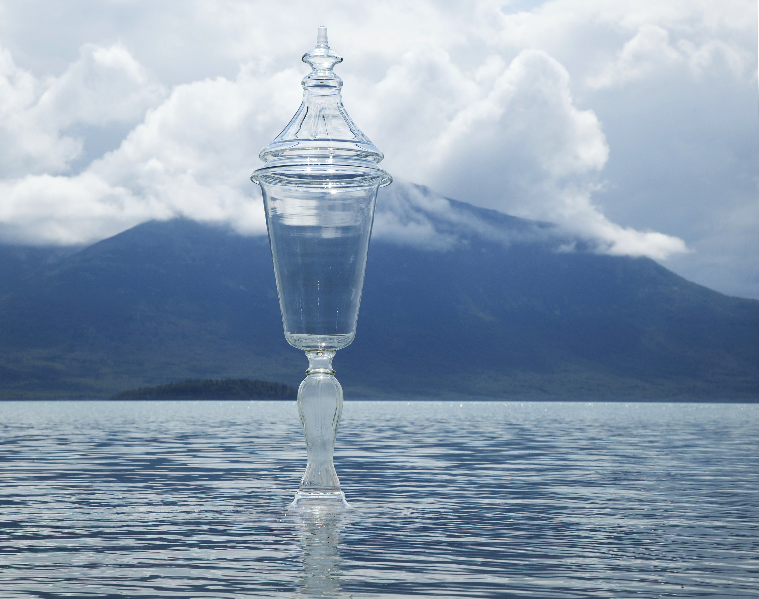 A glass chalice in a lake with a mountain in the background.