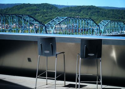 Two tall chairs at a bar on the balcony with the blue pedestrian bridge in the background.