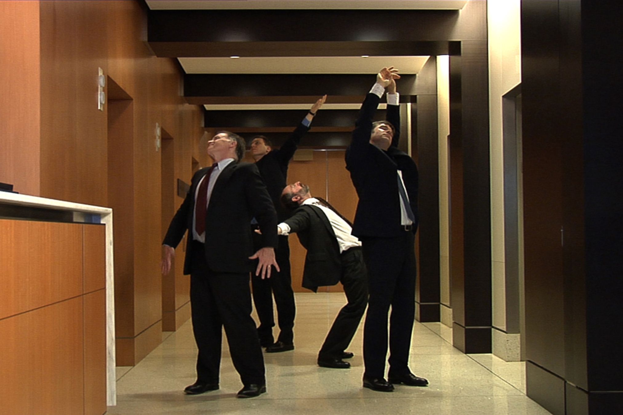 Men in suits stretch in a hall with wood panels.