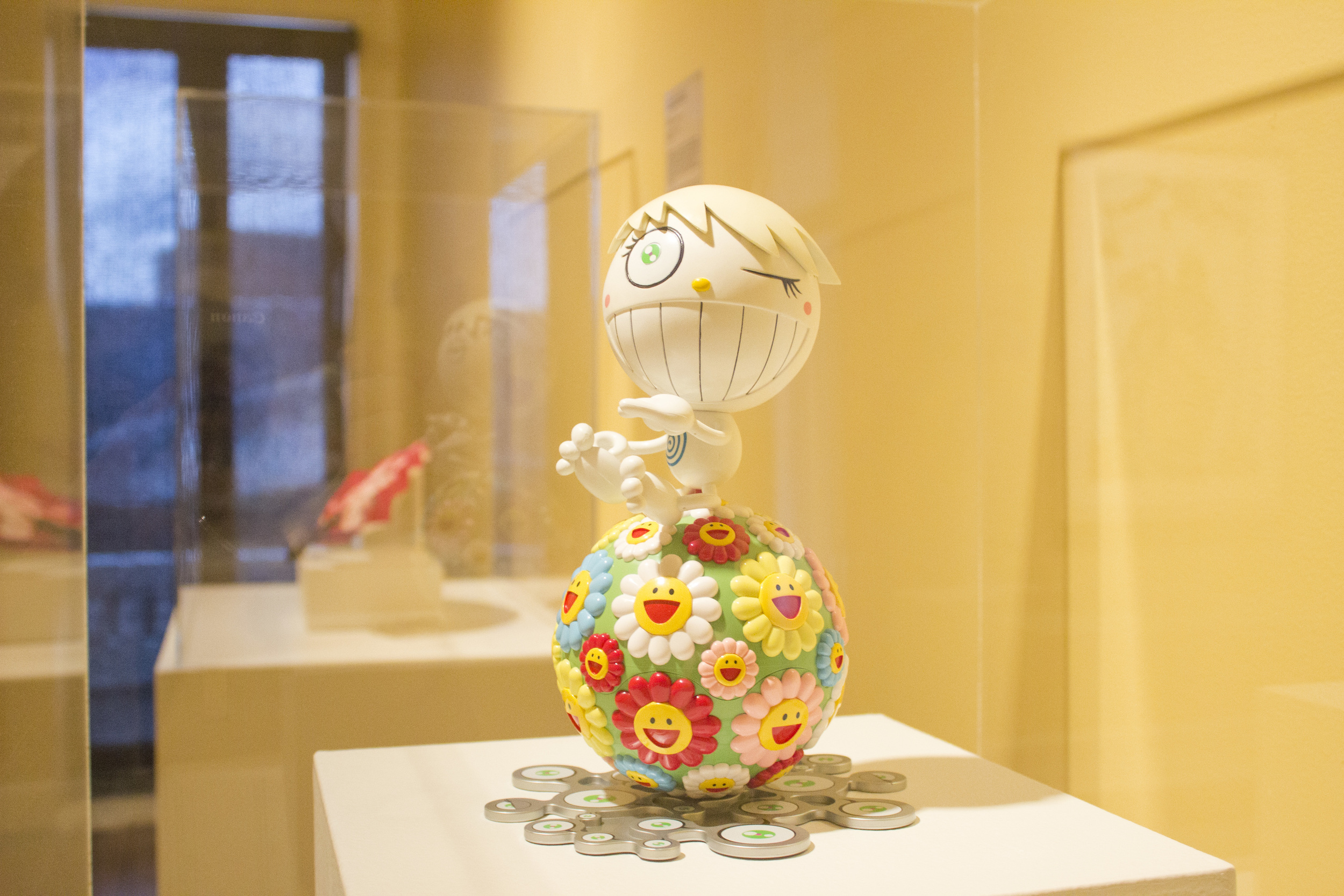 A case of a figure that is smiling and winking made from two balls. The lower section of the figure is covered in smiling flowers.