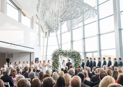 A wedding ceremony taking place in the lobby of the Hunter Museum. The bride and groom are at the altar with a tunnel of flowers behind them.
