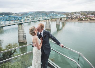 A bride and groom kiss on the balcony of the Hunter Museum with the pedestrian bridge lit up and the Tennessee river in the background.
