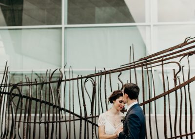 The groom is kissing his wife's forehead against an iron sculpture of rods of varying sizes.