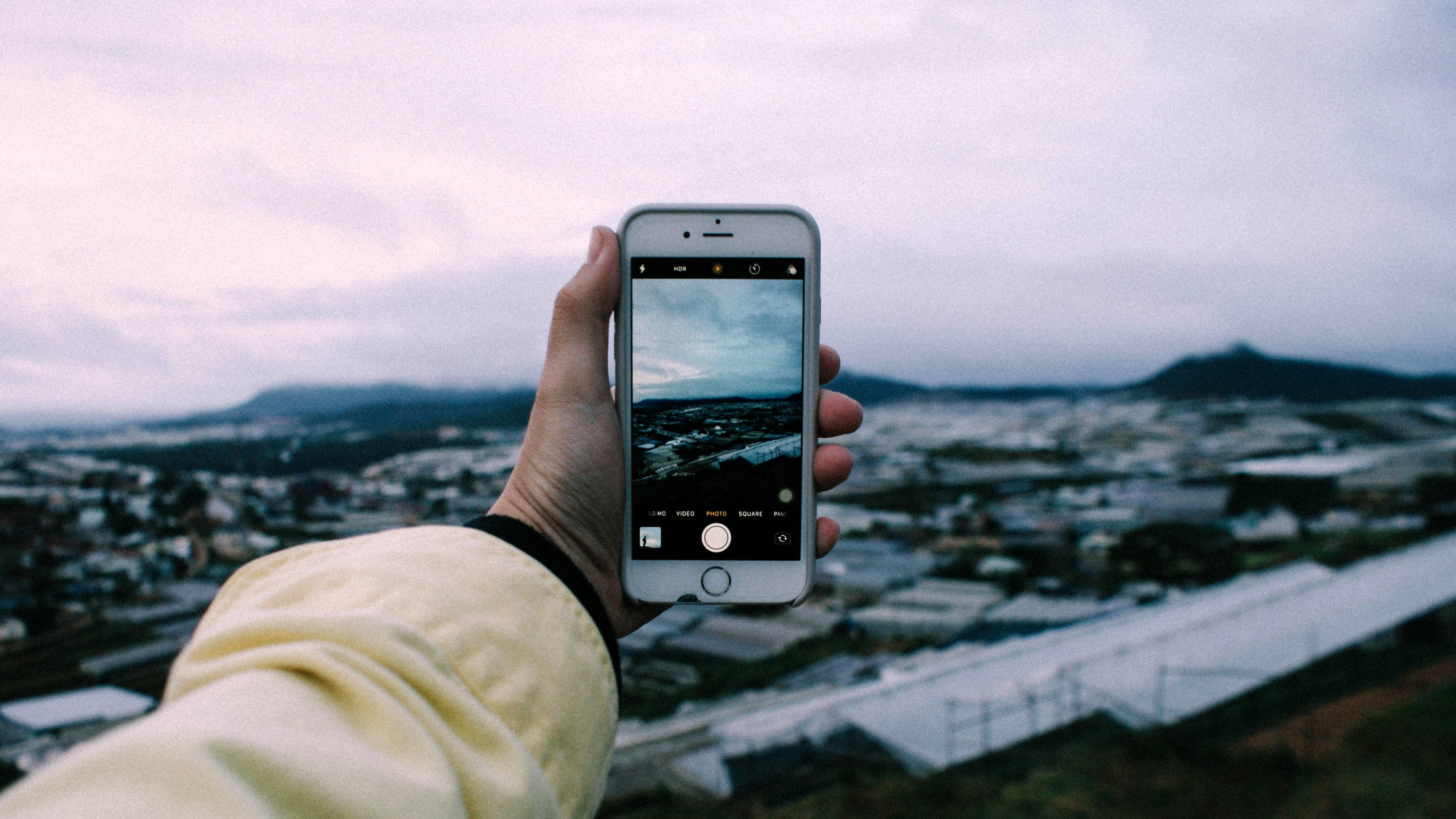 A person holds up a smartphone to take a picture of an urban landscape on an overcast day.