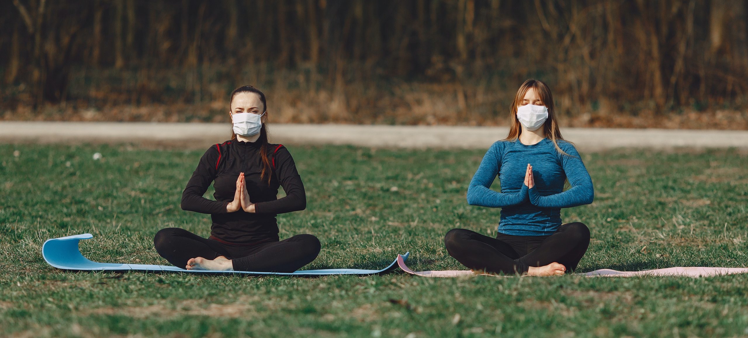 Two women do yoga outside. They are six feet apart and wear face masks.